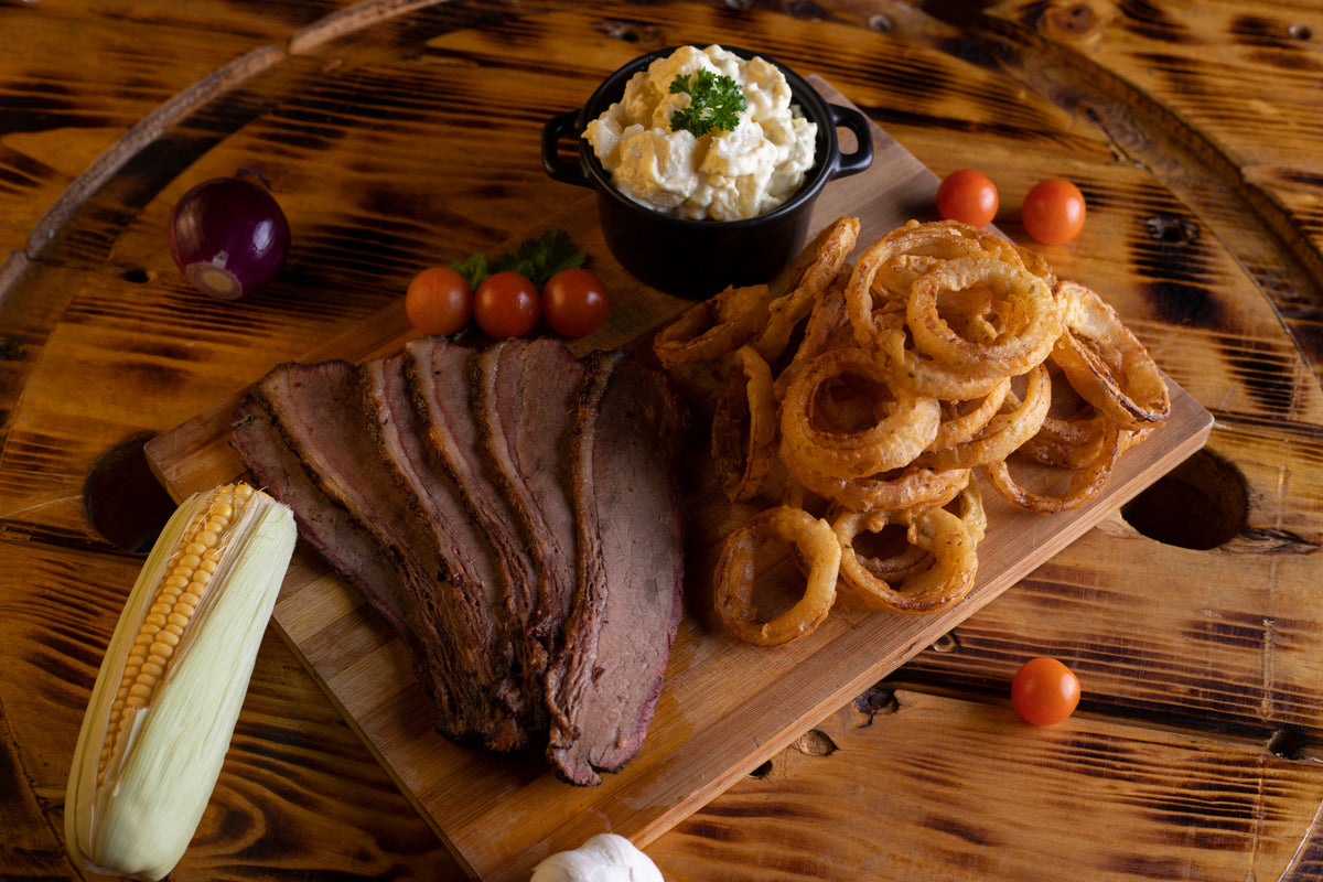 Sliced smoked brisket with onion rings and potato salad on wooden board