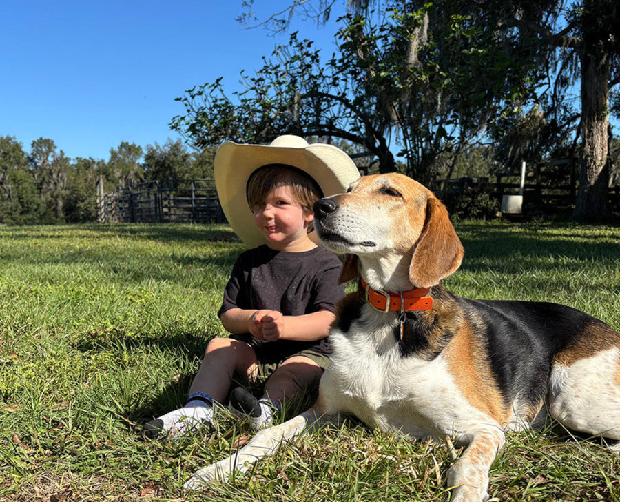 A child in a cowboy hat sitting in the grass with a dog at Riverbend Cattle Company