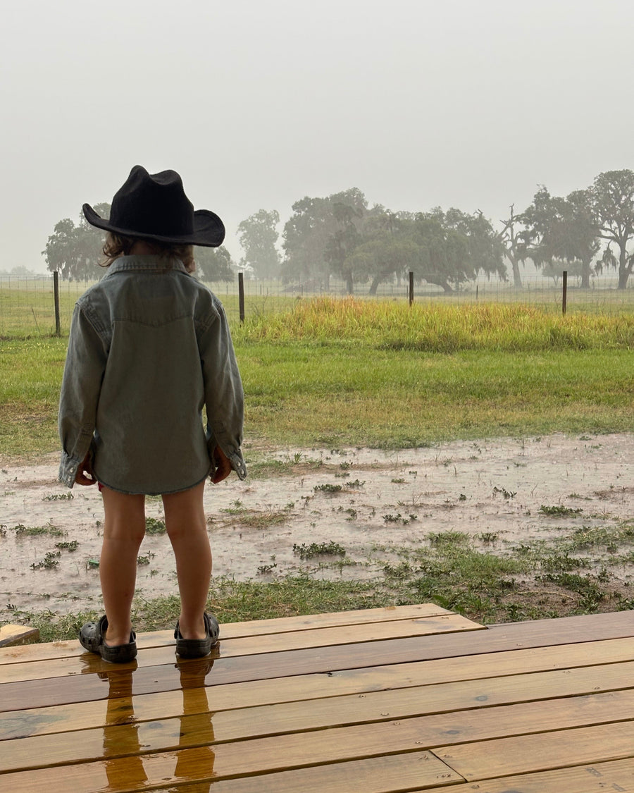 A child in a cowboy hat looking out over the pasture with cattle behind at Riverbend Cattle Company