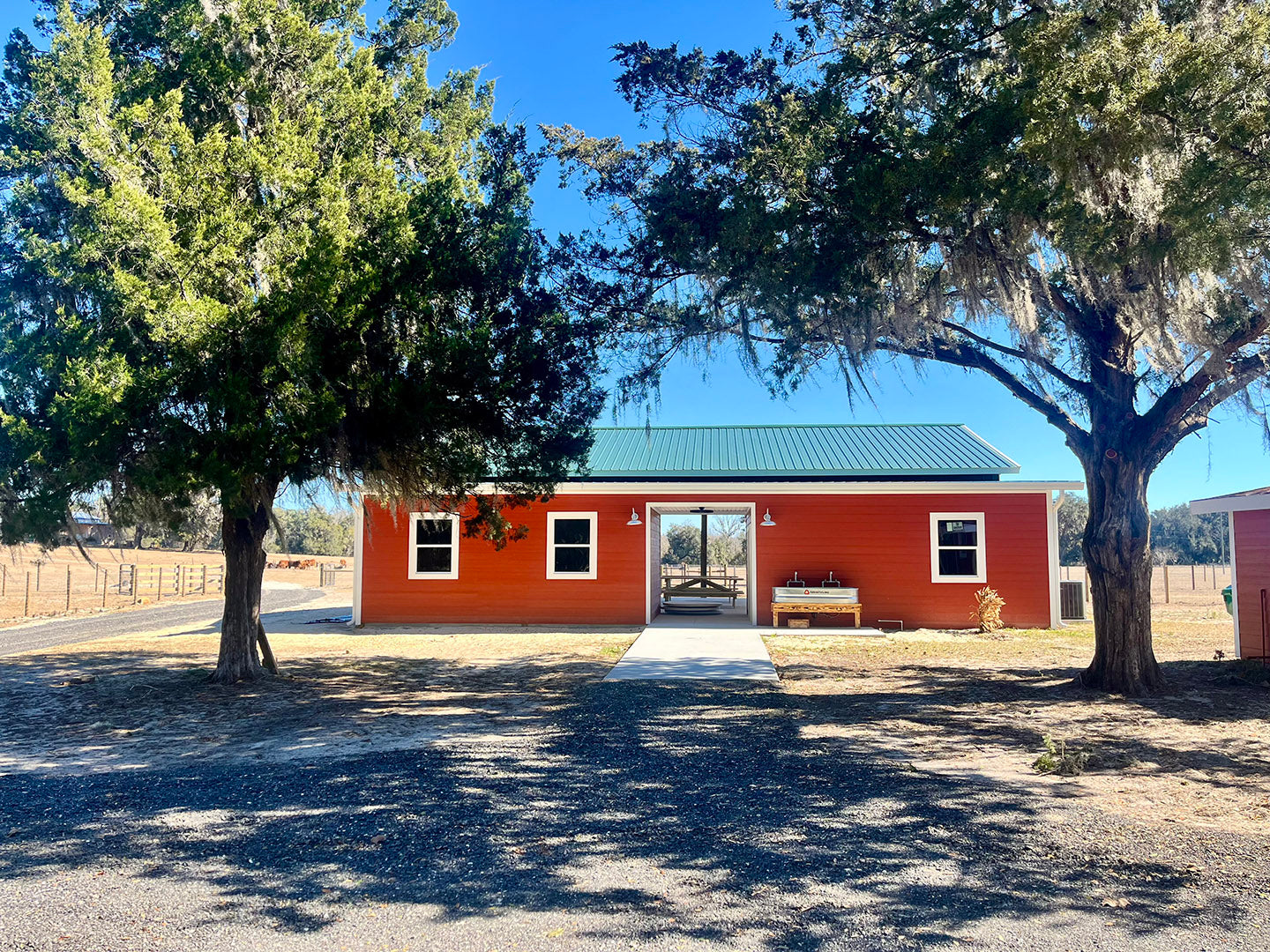 Red event barn and pavilion with kitchen, picnic tables, bathrooms and handwashing stations flanked by oak trees.